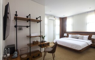 A hotel room with a bed, a desk with drawers, a chair, a TV, and a window with curtains.