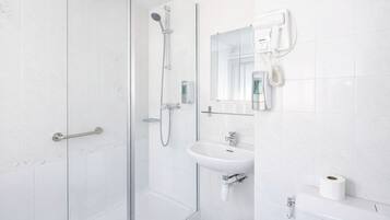 Un baño moderno con cabina de ducha de vidrio, un lavamanos blanco, un inodoro y un secador de pelo montado en la pared.