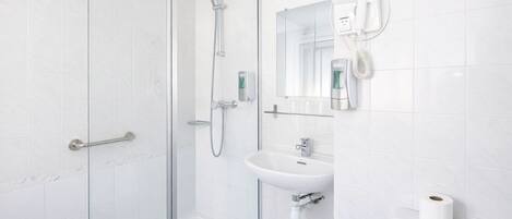 Un baño moderno con cabina de ducha de vidrio, un lavamanos blanco, un inodoro y un secador de pelo montado en la pared.