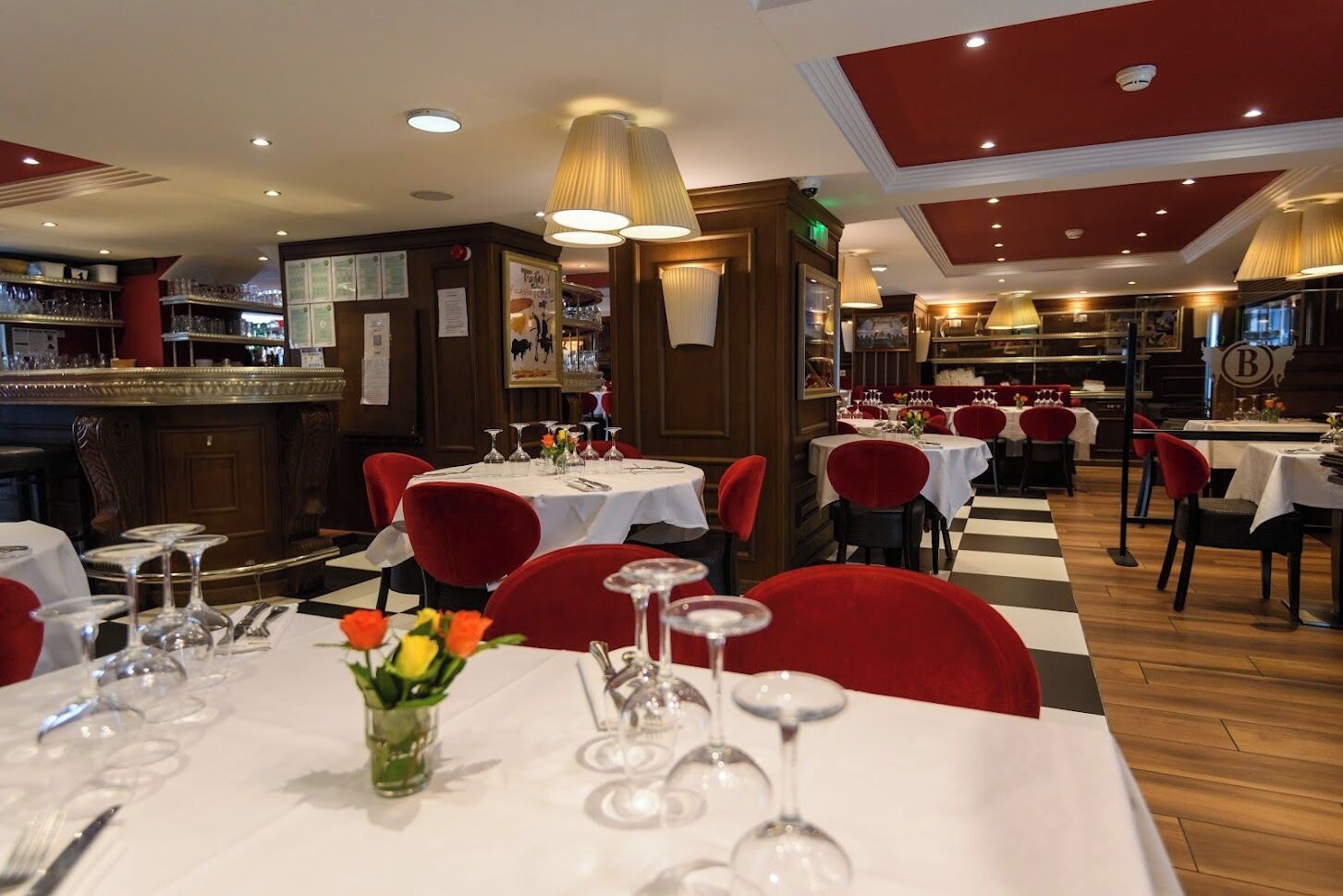En restaurant med flere borde, røde stole og et barområde.