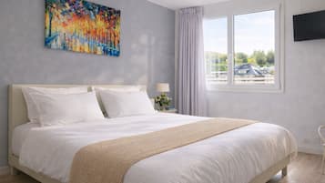 Un dormitorio con una cama grande, un cuadro en la pared, una ventana con cortinas y un televisor montado.