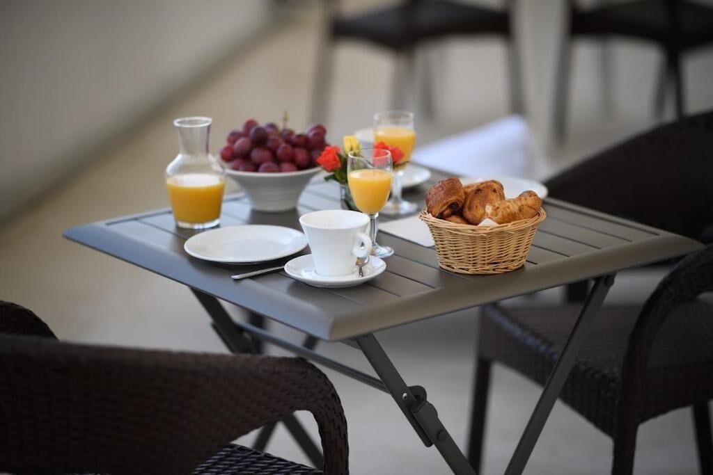 Un desayuno con una mesa, platos, una taza, una cesta de croissants, un bol de uvas y vasos de zumo de naranja.