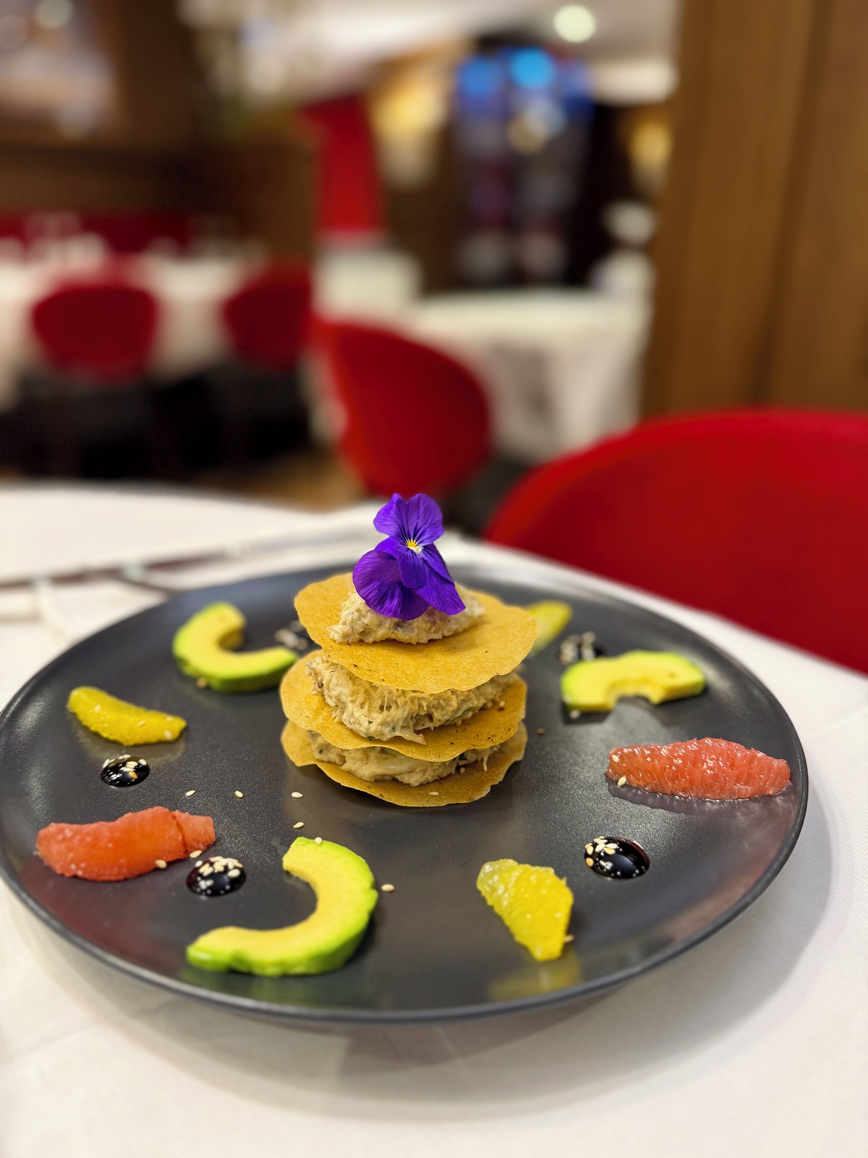 A plate with food items including avocado slices, a piece of salmon, and a decorative purple flower.