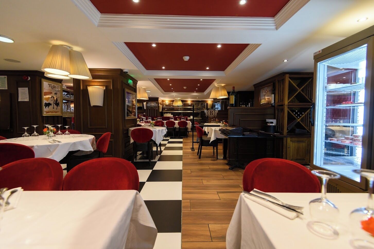 Un restaurante con mesas dispuestas para comer, un suelo a cuadros y vistas a la cocina a través de una puerta de cristal.