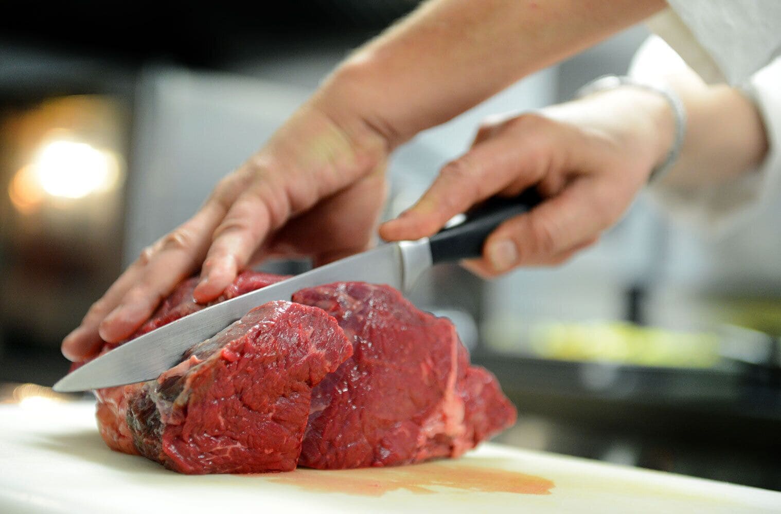 Une personne qui découpe une grande portion de viande crue sur une planche à découper.