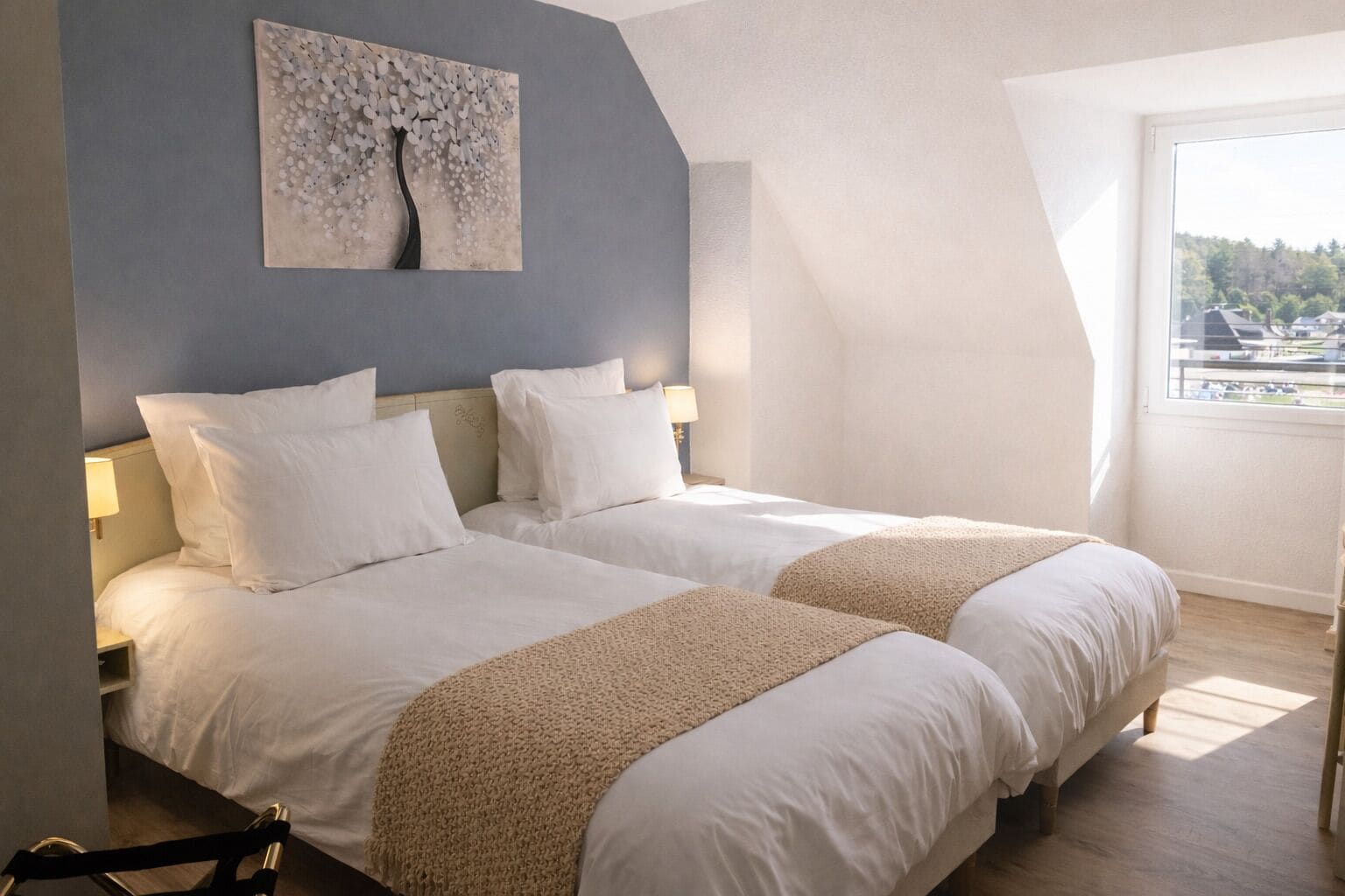 Camera d'albergo moderna con due letti, un'ampia finestra vista e un'opera d'arte originale al soffitto.