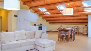 Una sala de estar acogedora con un sofá seccional blanco, una mesa de comedor de madera con sillas, y una zona de cocina con armarios y electrodomésticos.