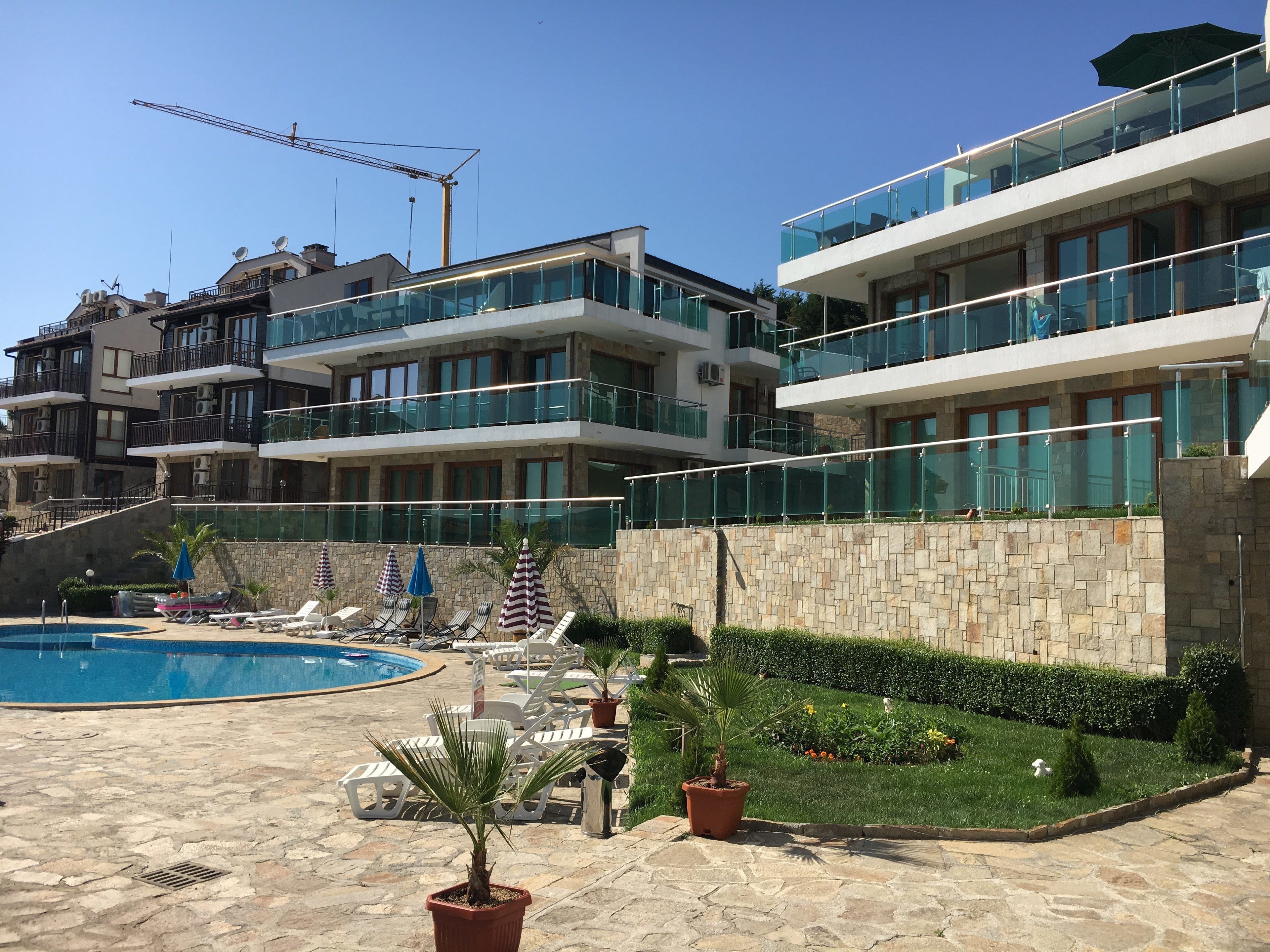 A modern hotel with a swimming pool, multiple balconies, and a well-maintained garden.