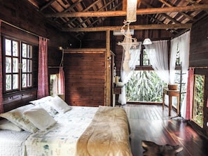 Un dormitorio de cabaña de madera con cama, almohadas, una lámpara colgante y vistas al exterior.