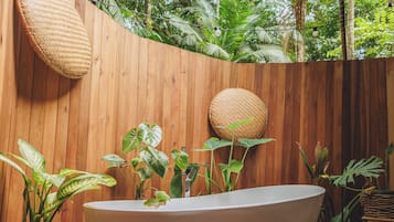 Una terraza de madera con una bañera independiente rodeada de macetas con plantas diversas.