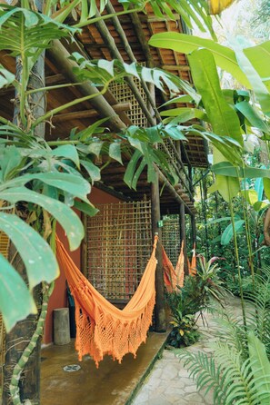 A hammock suspended between a bamboo structure and a thatched roof, surrounded by lush tropical foliage.