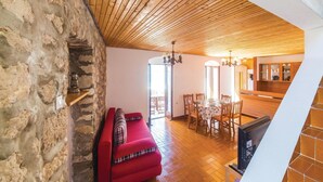A cozy living room with a red sofa, wooden ceiling, stone wall, and a dining area with a table and chairs.