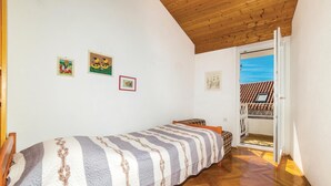 A small, single-bed room with a wooden ceiling, a balcony with a tiled roof, and three framed pictures on the wall.