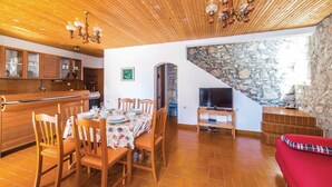 A cozy living room with a wooden ceiling, a stone wall, a dining area with a table set for four, and a red sofa.