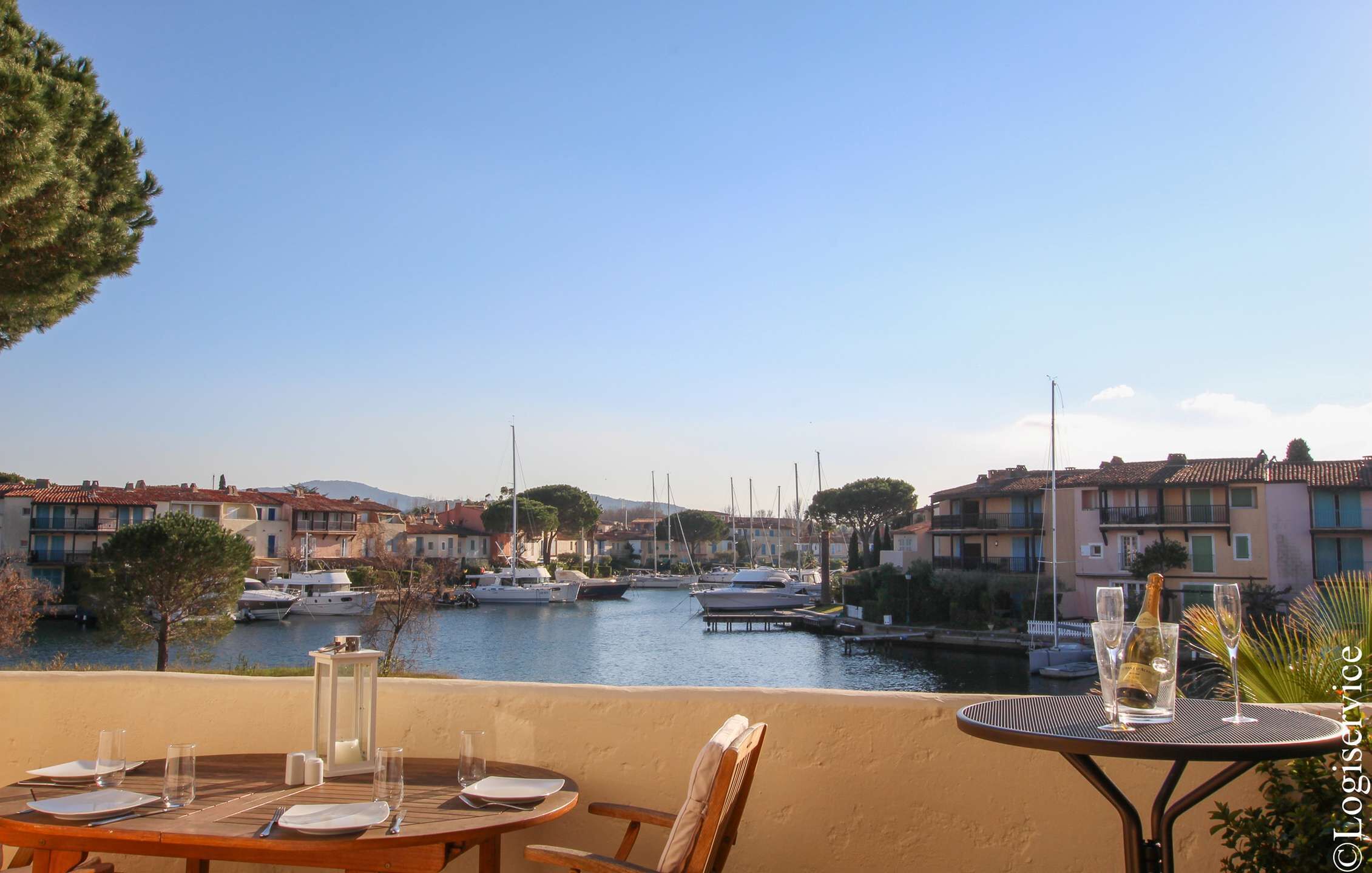A terrace with a table set for dining, overlooking a marina with boats and buildings.