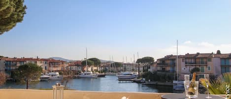 A terrace with a table set for dining, overlooking a marina with boats and buildings.