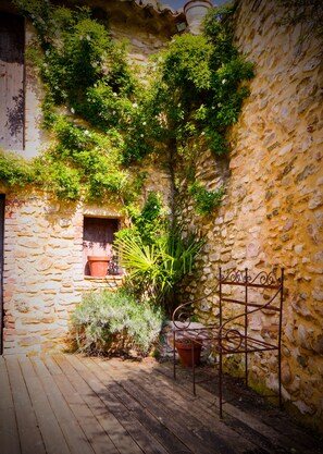 A stone building with a wooden deck, potted plants, and a metal gate.