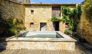 Un cortile con una piscina in pietra, pareti in pietra, porte in legno e piante in vaso.