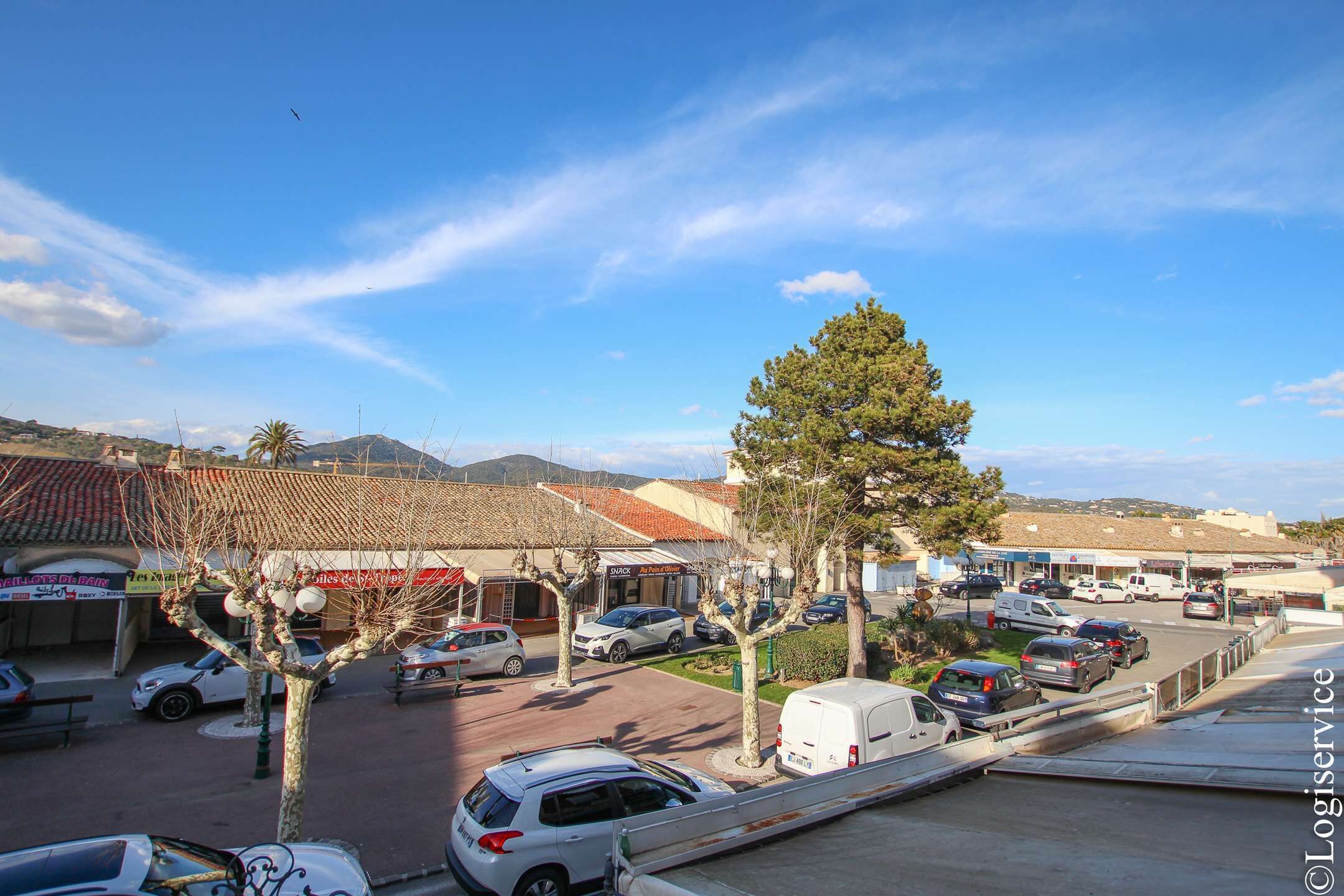 A parking lot with several cars, a few trees, and buildings with signage in the background.