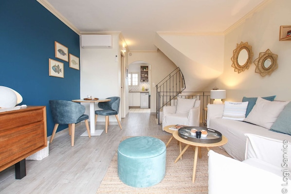 A modern living room with a sofa, a coffee table, and a blue ottoman. There is a staircase leading to an upper floor. - Duplex flat 4/6 persons Port Grimaud (PORT GRIMAUD)