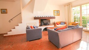 Una sala de estar con chimenea, dos sofás, un televisor y una escalera.