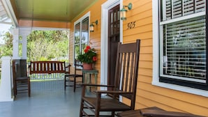 A porch with wooden rocking chairs and a table, a potted plant with red flowers, and a house number 505.