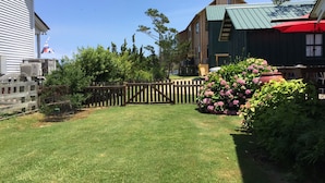A well-maintained grassy yard with a wooden fence, a wooden deck, and a variety of plants and flowers.