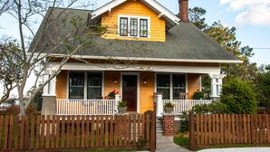 A two-story house with a yellow facade, white trim, and a front porch with a wooden fence.
