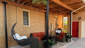 Une terrasse couverte avec des meubles en osier, un fauteuil suspendu et une porte rouge.