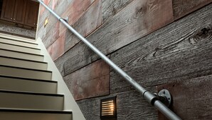 Un escalier avec une rampe métallique adossé à un mur en bois rustique.