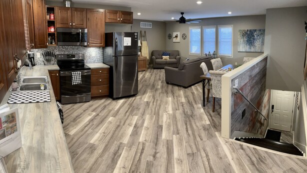 Une cuisine moderne avec des meubles en bois, des appareils en acier inoxydable et un parquet gris à motifs chevrons.