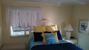 Una camera da letto con un letto, un comodino con una lampada, una finestra con tende e un termosifone.