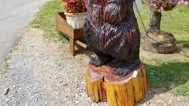 A wooden bear sculpture with outstretched arms, a wooden bench, and a flower planter. - Condo located in the heart of Pigeon Forge, TN   3603 Plaza Drive (Pigeon Forge)