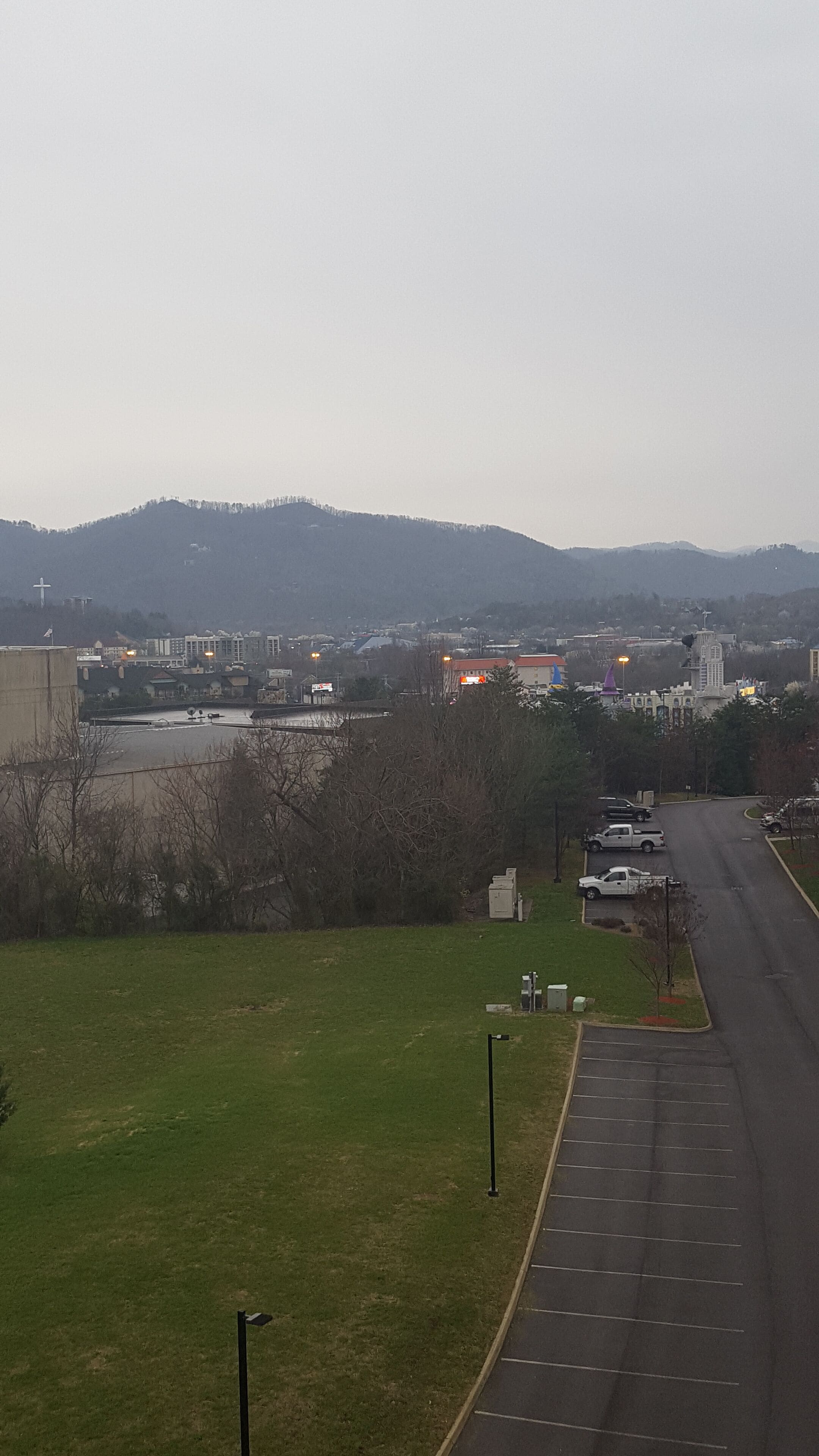 A parking lot with a grassy area and a road leading to a town.