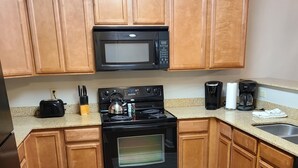 A kitchen with wooden cabinets, a black microwave, a stove, a coffee maker, and a sink. - Condo located in the heart of Pigeon Forge, TN   3603 Plaza Drive (Pigeon Forge)