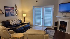 A living room with a dark wood floor, a ceiling fan, a fireplace, and a television mounted on the wall. - Condo located in the heart of Pigeon Forge, TN   3603 Plaza Drive (Pigeon Forge)