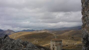 A mountainous landscape with a small building, possibly a chapel, surrounded by rocky terrain and distant hills.