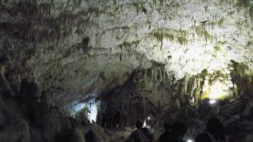 A cave interior with stalactites and stalagmites, illuminated by artificial light.