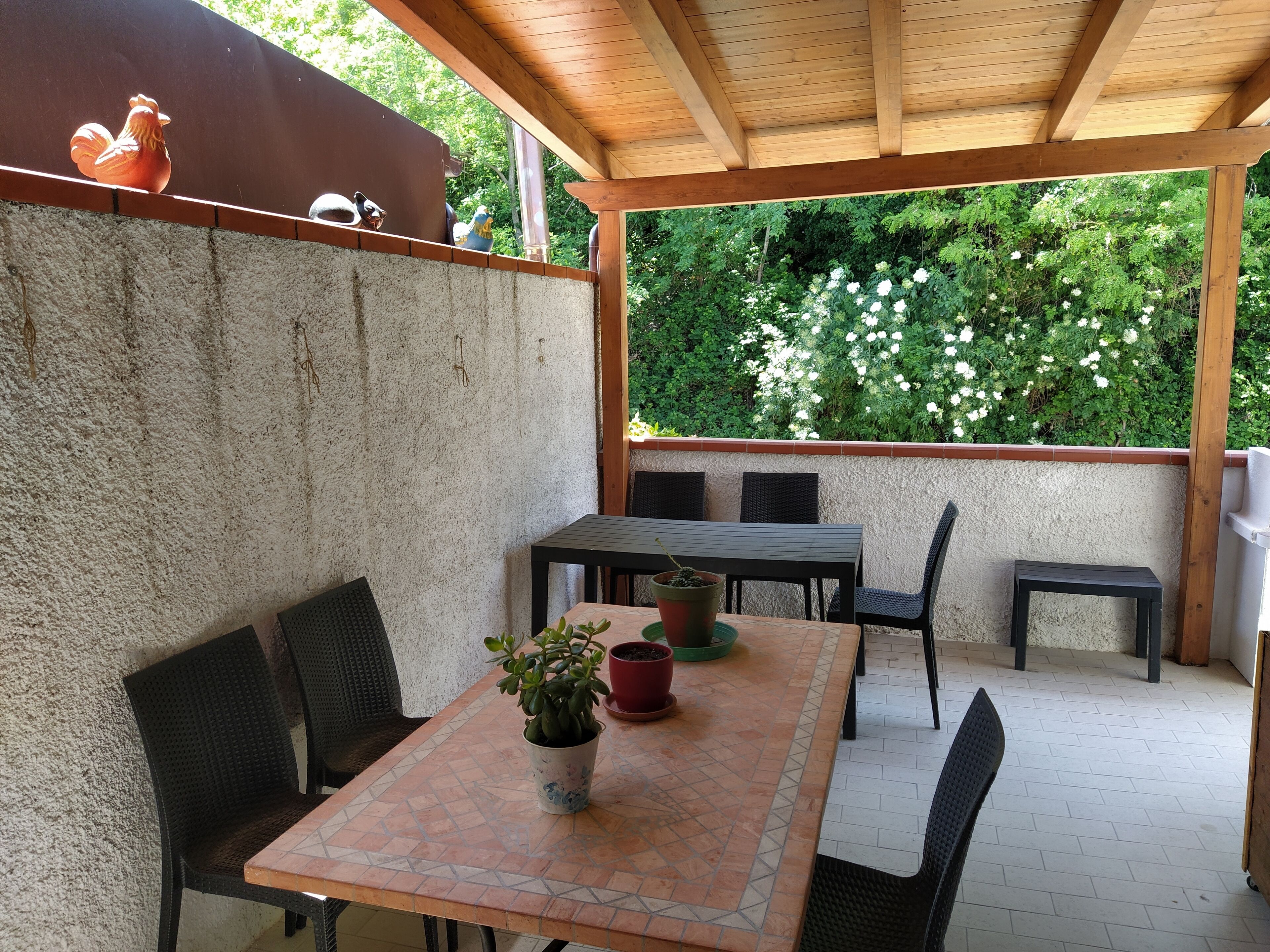 An outdoor patio with a wooden pergola, a tiled table, and chairs.