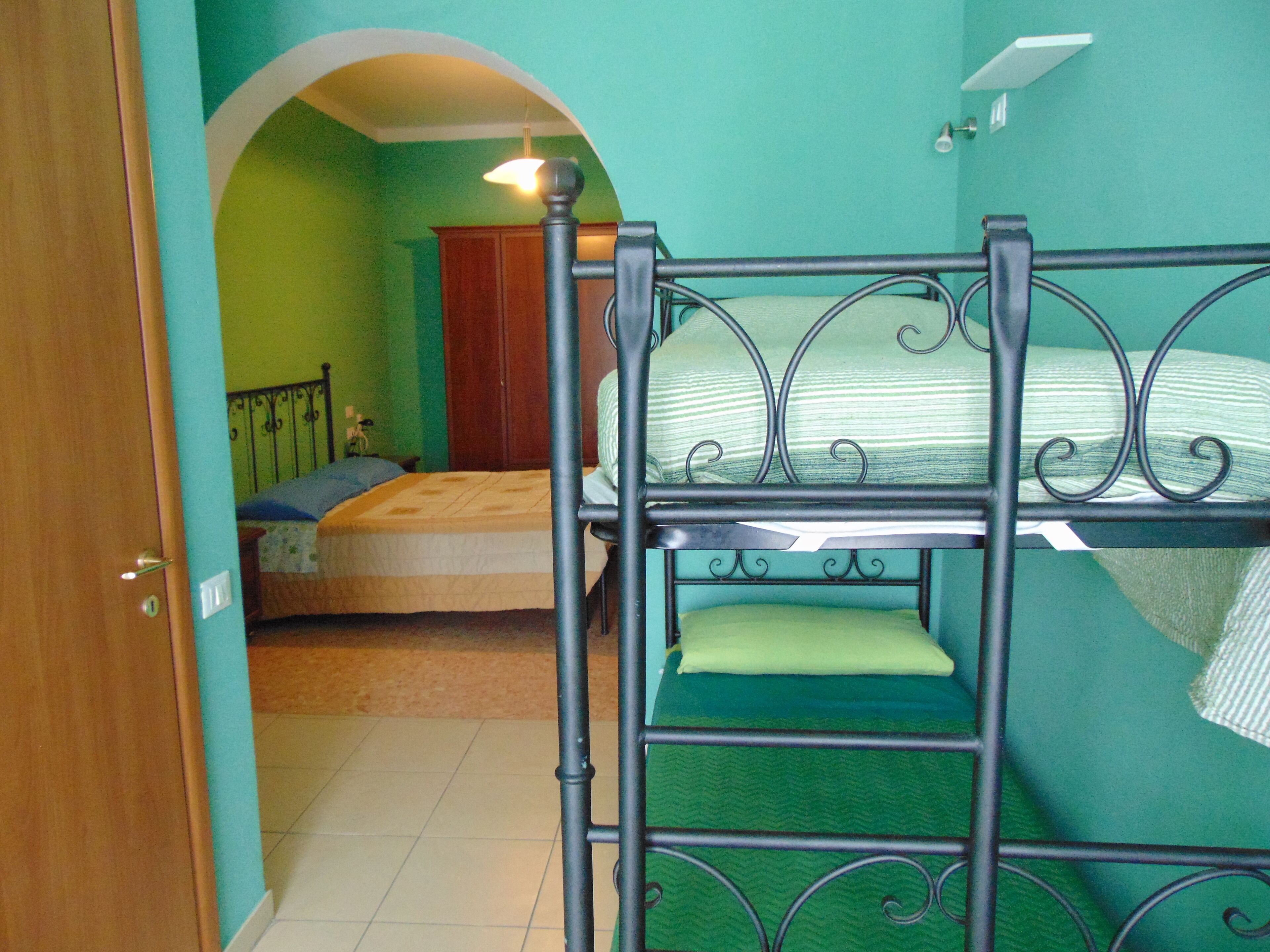 Una stanza con letti a castello, una porta in legno, un muro verde e un pavimento piastrellato.