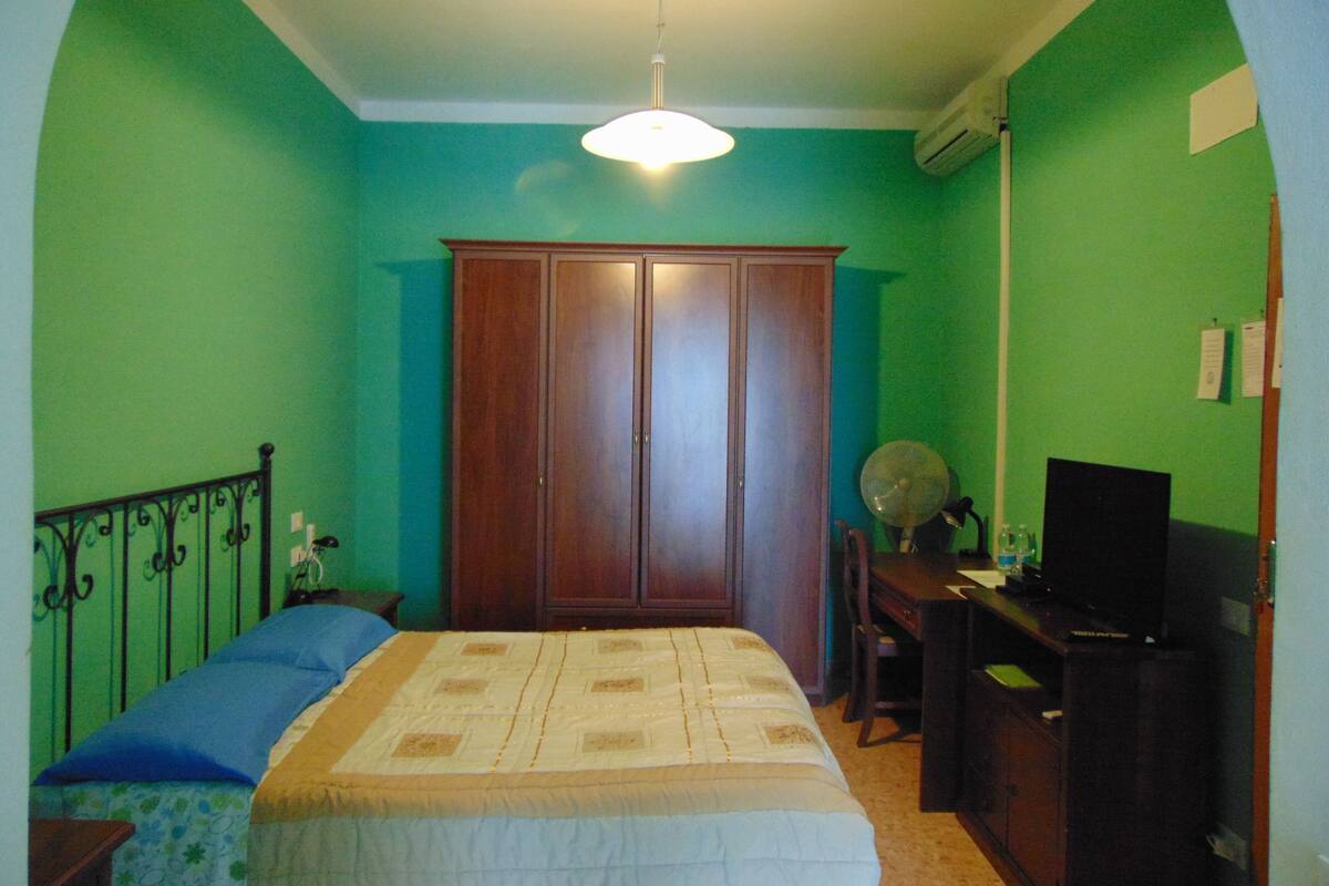 A bedroom with a bed, a wardrobe, a desk, and a television.