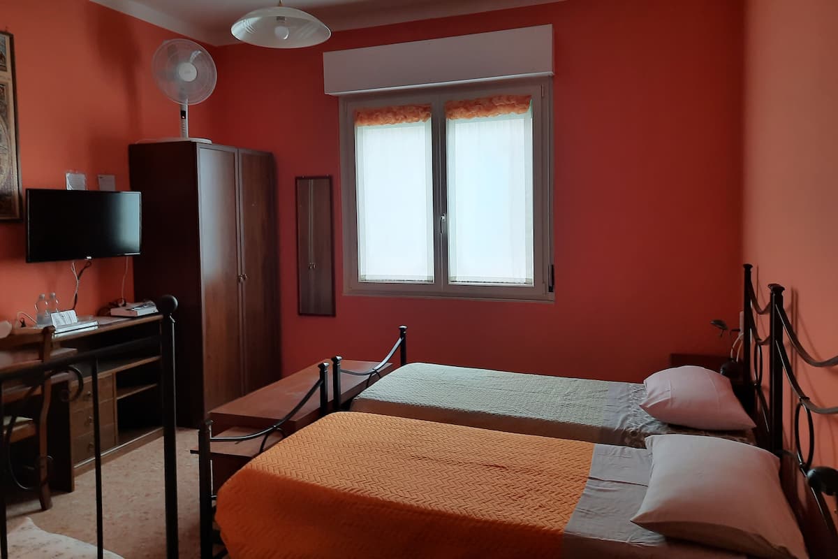 A bedroom with a bed, a desk, a chair, a wardrobe, and a window with curtains.