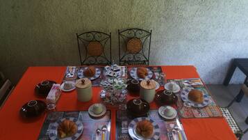 Une table dressée avec des croissants, du café et du thé, agrémentée d’un chemin de table à motifs et de chaises en métal.