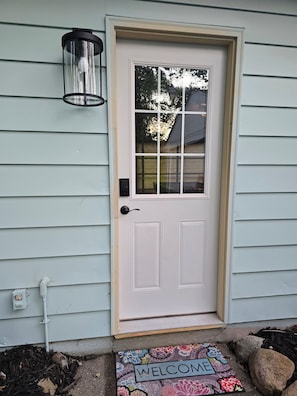 A white door with a glass panel, a black outdoor light fixture, and a welcome mat with floral patterns.