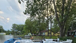 Un barco amarrado en un muelle de madera, con una casa y árboles al fondo.