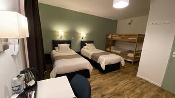 A hotel room with two beds, a desk with a coffee maker, and a bunk bed.