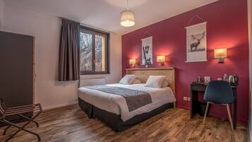 Un dormitorio con suelo de madera, una cama con edredón gris y blanco, un escritorio con silla y una ventana con cortinas.
