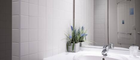 A bathroom with white tiled walls, a white sink, a mirror, and a shower area.