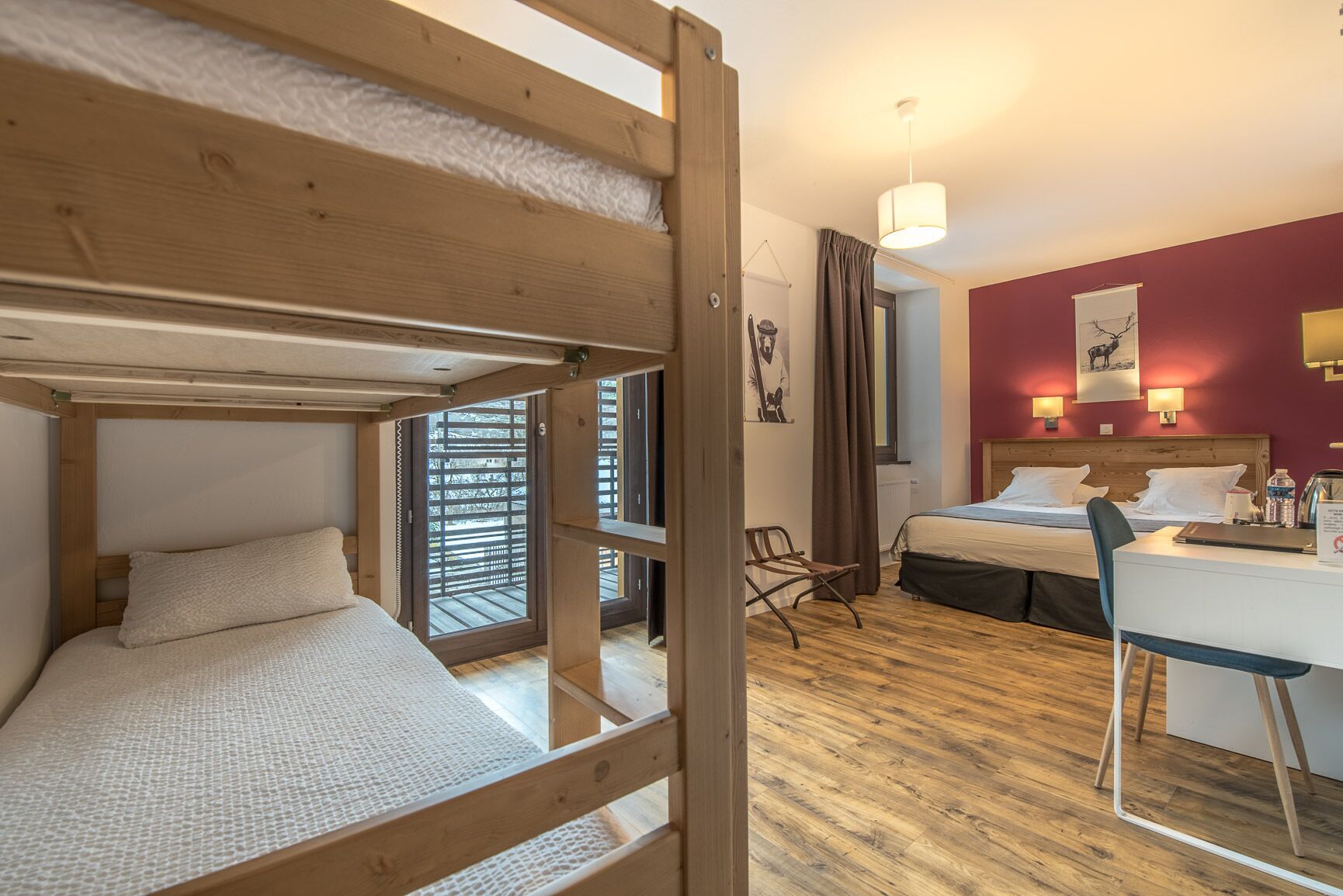 Une chambre avec un lit superposé, un bureau et une chaise. Il y a une fenêtre avec des stores, une lampe et un tableau au mur.