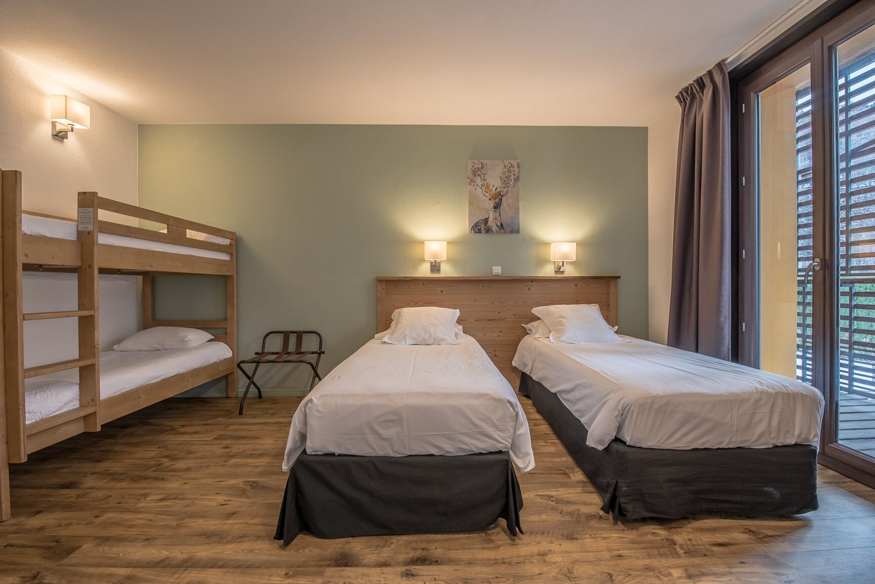 A room with two single beds, a bunk bed, a wooden floor, and a painting on the wall.